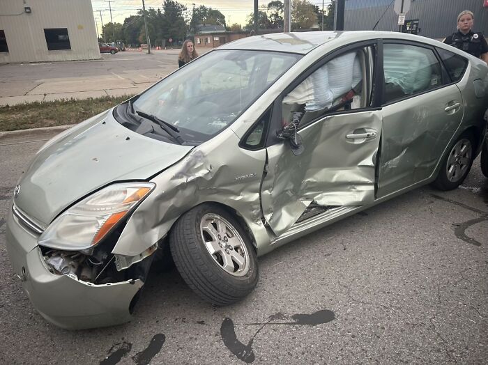 Damaged silver car with crushed front left side and rear door, police and bystander nearby after a severe accident survival situation.