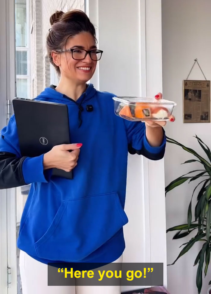 Woman in blue hoodie holding food container and laptop, illustrating Bulgarian and Dutch food sharing culture contrast. Woman in blue hoodie holding food container and laptop, illustrating Bulgarian and Dutch food sharing culture contrast.
