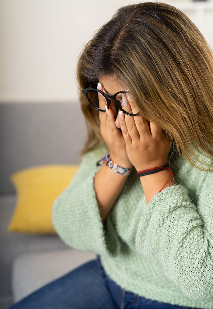 Woman covering face in distress, upset after coworker offers old clothes not fitting her skinny frame, emotional reaction at home. Woman covering face in distress, upset after coworker offers old clothes not fitting her skinny frame, emotional reaction at home.