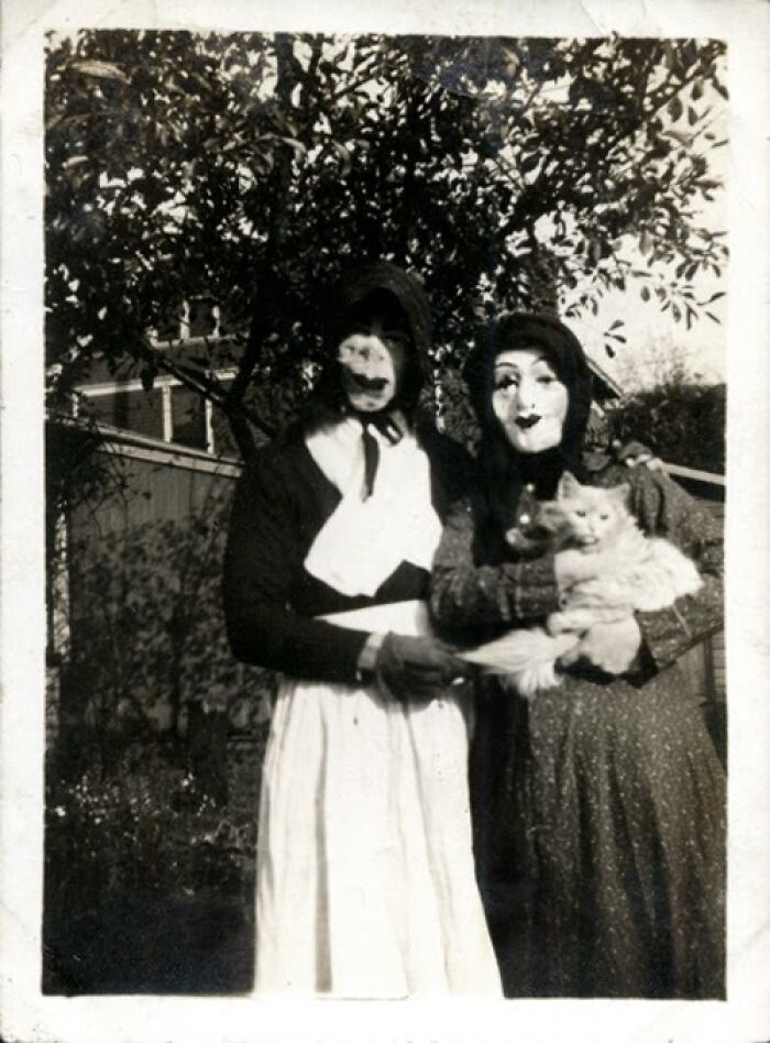 Vintage Halloween costumes from the past featuring eerie masks and classic fabric dresses in a black and white photo.