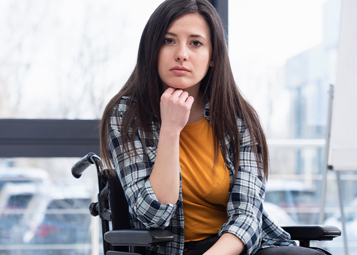 Paralyzed woman in wheelchair looking thoughtful and serious indoors reflecting on social life and babysitting refusal.