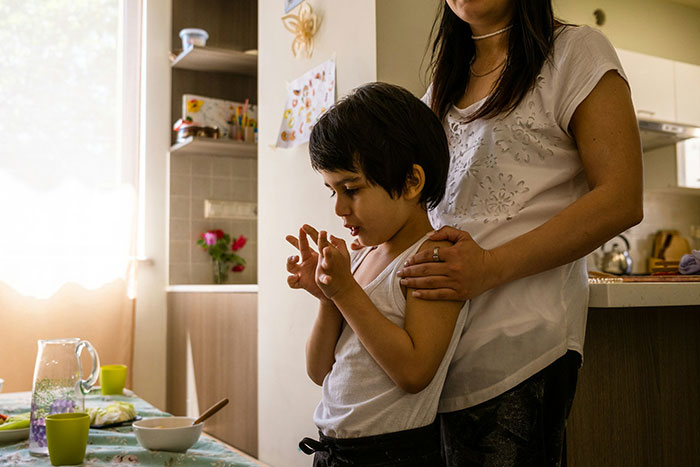 Teen and parent in kitchen after cake fail, showing mixed emotions and supportive embrace from adult.