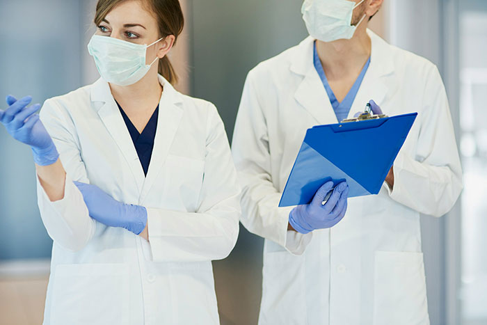 Two doctors wearing masks and gloves in a medical practice discussing a situation involving lost costs and family conflict.