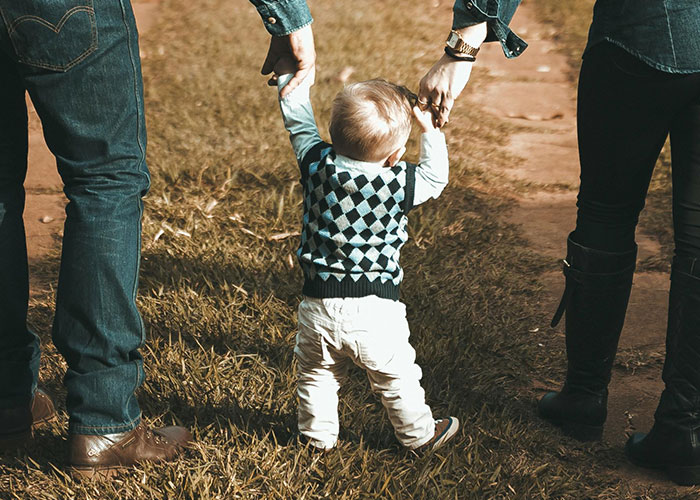 Toddler walking with parents holding hands on a grassy path, highlighting a story about illegal baby adoption and CPS report. Toddler walking with parents holding hands on a grassy path, highlighting a story about illegal baby adoption and CPS report.