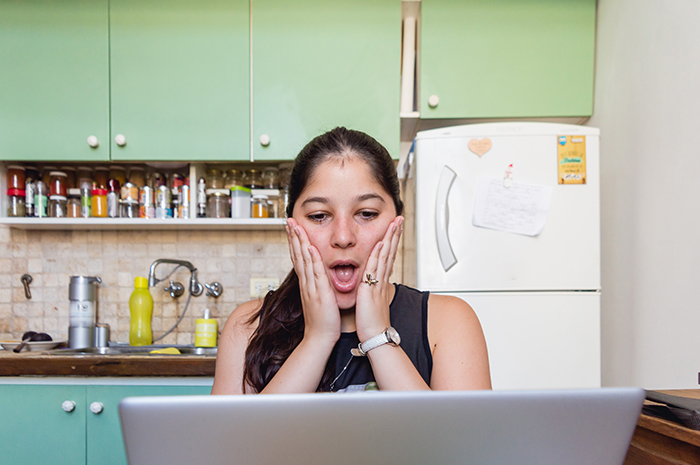 Teen reacting in shock at laptop in kitchen, showing disbelief over stepmom&rsquo;s hypocrisy and lies online.