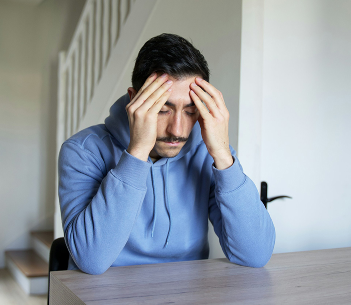 Stressed man sitting at table holding his head, reflecting family conflict over caring for disabled sister and ableist accusations. Stressed man sitting at table holding his head, reflecting family conflict over caring for disabled sister and ableist accusations.