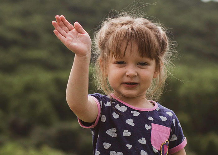 Young child waving outdoors, illustrating a moment that could embarrass moms as shared in stories about kids embarrassing parents.