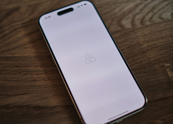 Smartphone displaying Airbnb app on wooden table, related to family rushes out of rental house after discovery.