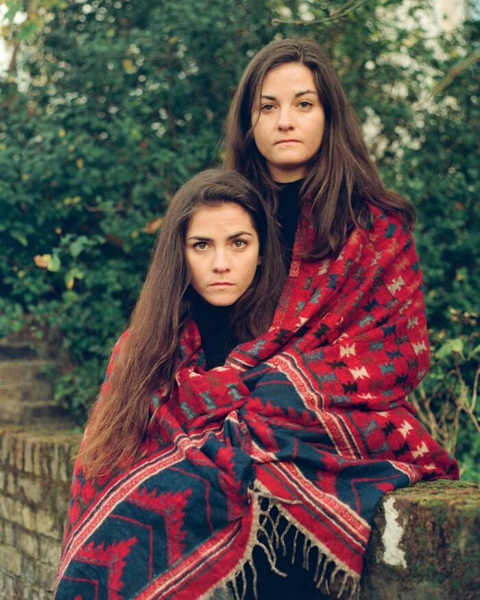 Two twins wrapped in a red patterned blanket in a garden, captured by a London photographer in a stunning portrait.