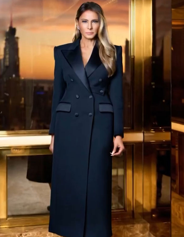 Melania Trump in a long black coat posing indoors with cityscape at sunset, linked to bizarre AI video conspiracy theory.