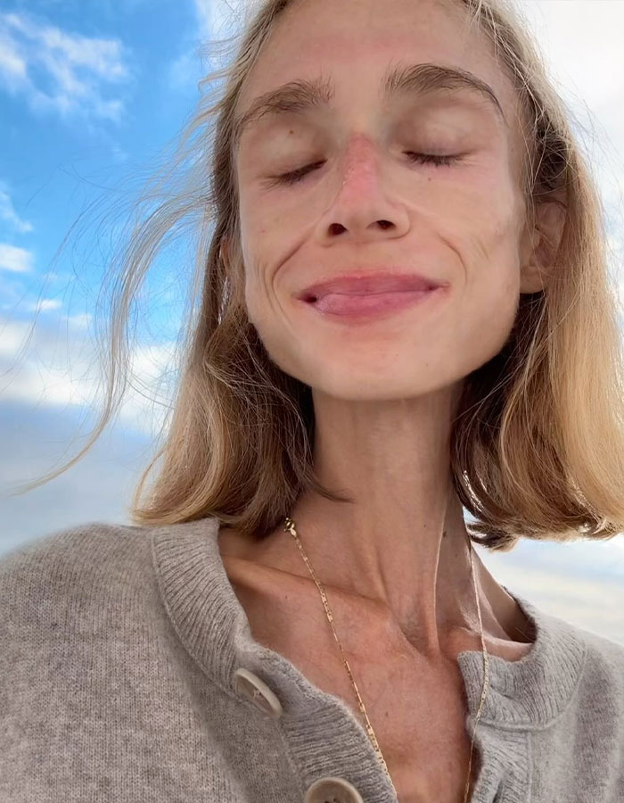 Vegan woman with closed eyes, wearing gray sweater and gold necklace, posing outdoors under blue sky. Vegan woman with closed eyes, wearing gray sweater and gold necklace, posing outdoors under blue sky.
