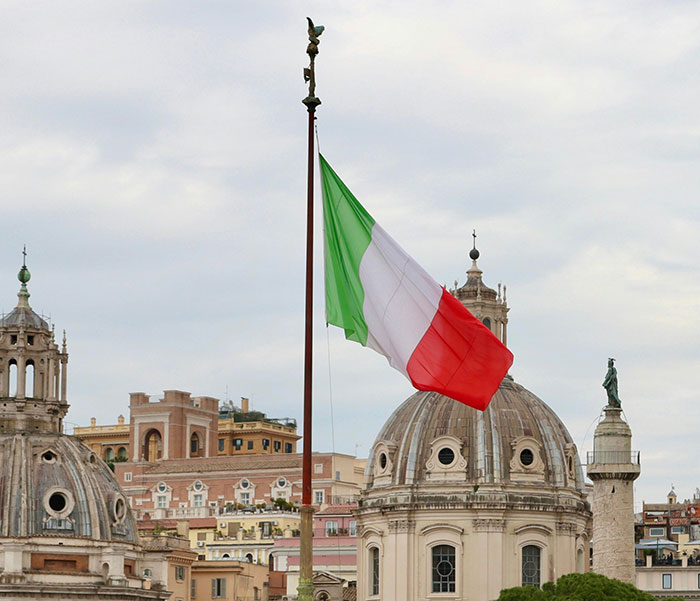 Italian flag flying over historic cityscape as American tourist requests Olive Garden dish in Italy.