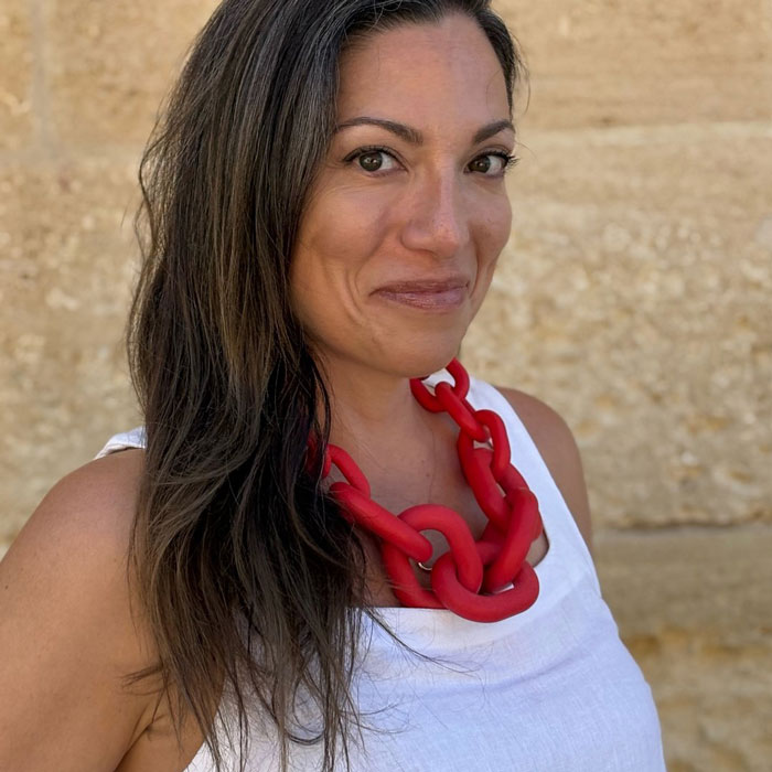 Woman with long dark hair and red necklace, recalling vacation regrets after using Meta glasses to record footage.