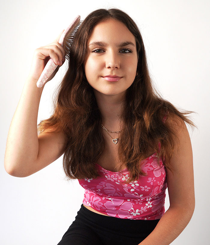 Young girl brushing hair in a pink floral top, representing 12YO who lost her life subway surfing, sparking parent blame online.