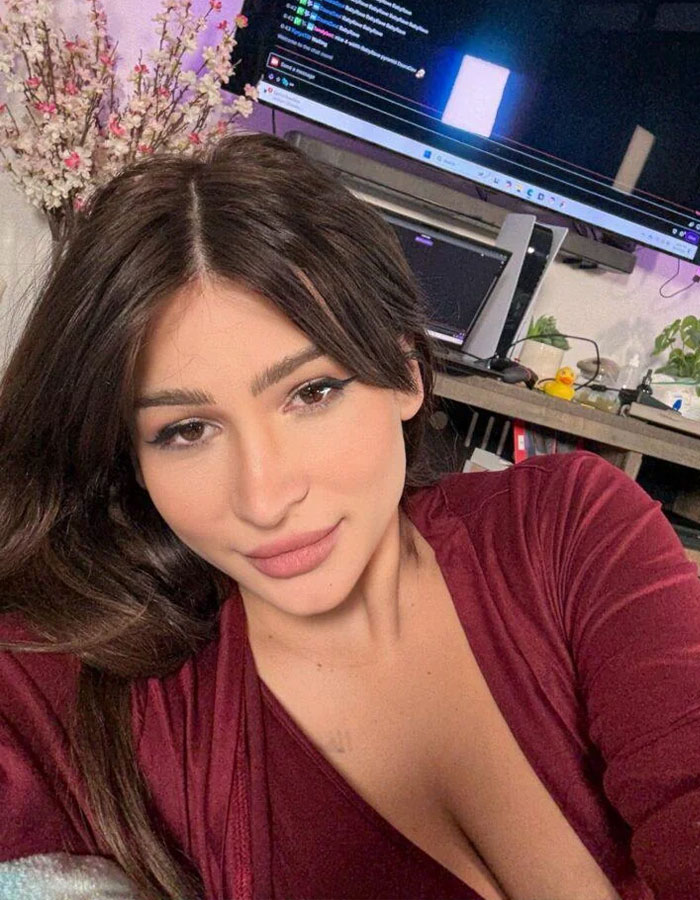 Young woman giving birth on Twitch livestream shown in a cozy room with computer screens and flowers in the background.