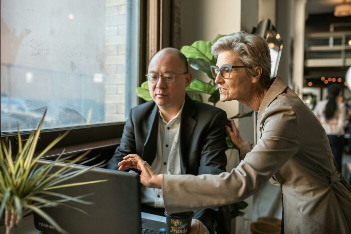 Two colleagues discussing unpopular opinions poll results while working on a laptop in a cozy cafe setting.