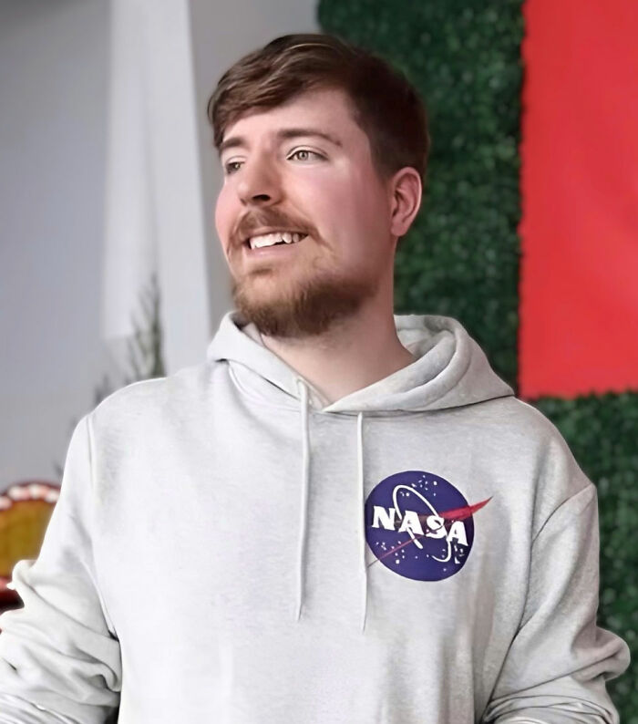Young man in a white NASA hoodie smiling indoors, illustrating people sharing celebs they can’t stand despite popularity.