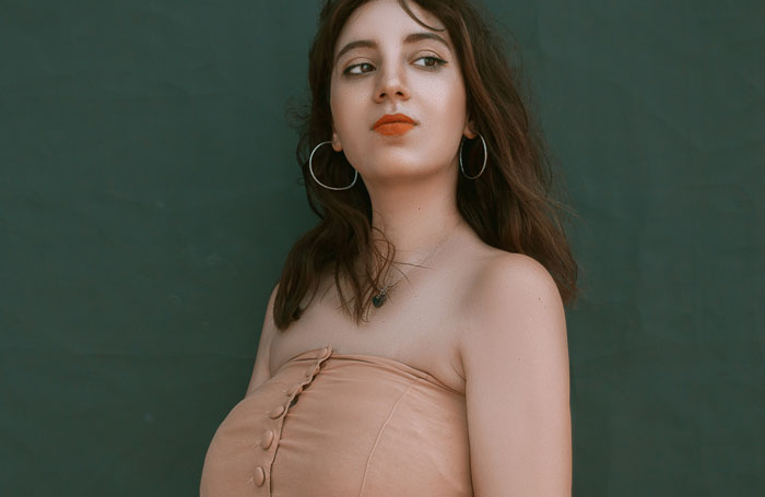 Young woman with hoop earrings and orange lipstick posing against a dark background for plastic surgeons insights.