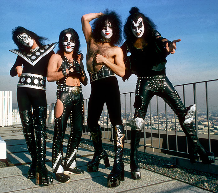 KISS band members Gene Simmons and Paul Stanley in iconic makeup and costumes posing on rooftop with city backdrop.