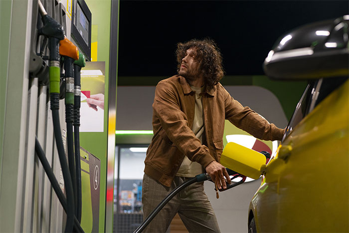Man with curly hair pumping gas into yellow car at night, evoking unexplainable creepy things experienced concept.