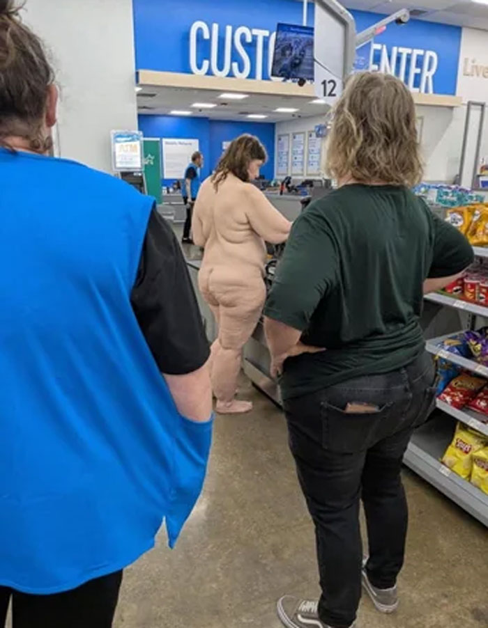 A naked woman standing at the checkout counter inside a Walmart with other shoppers nearby.