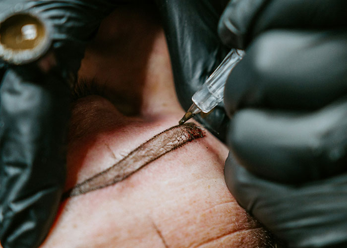 Close-up of a cosmetic procedure being done on an eyebrow with a handheld tool, highlighting cosmetic procedure risks.