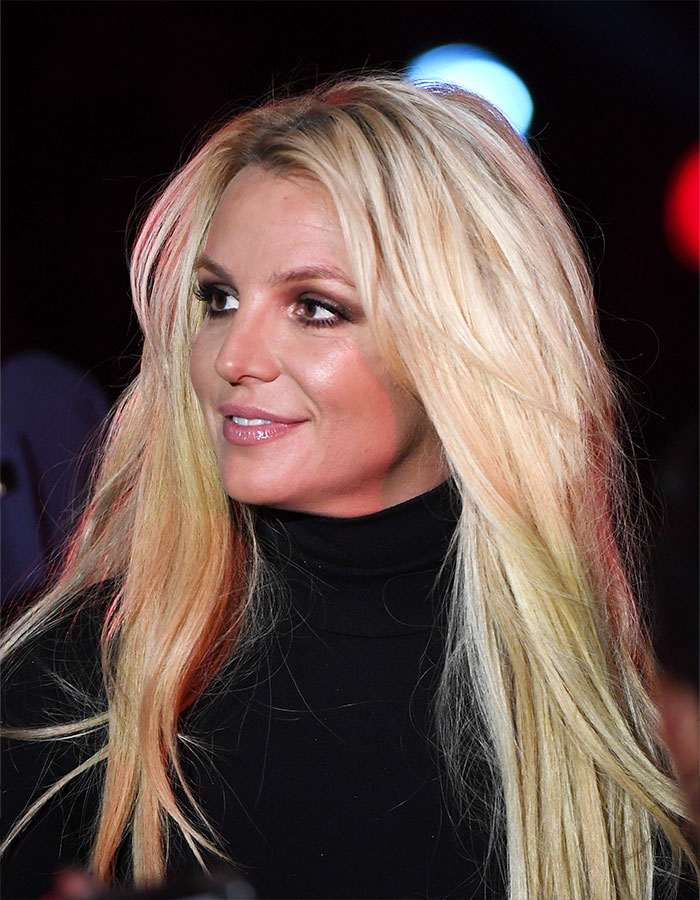 Britney Spears with long blonde hair and black turtleneck during a public appearance, related to brain damage confession.
