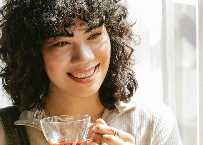 Young woman smiling and holding a cup of tea near a window, illustrating psychologists debunking mental health myths.