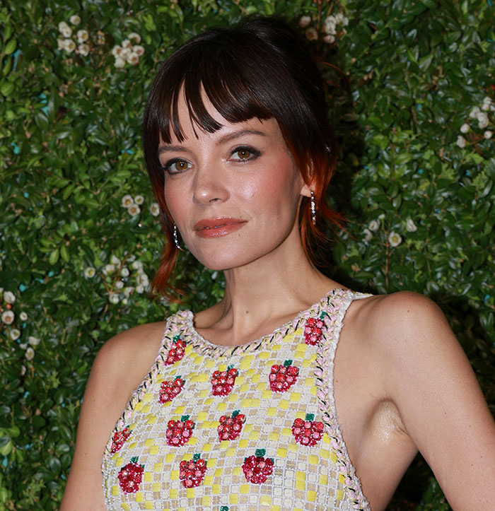 Woman posing in a floral dress with red accents, representing fans clash online over David Harbour cheating controversy.