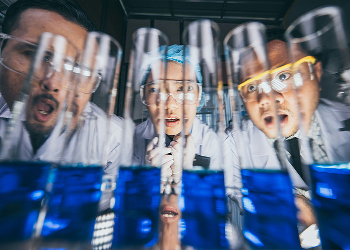 Three scientists wearing lab coats and safety goggles examining blue liquid in test tubes during an experiment about breathing. Three scientists wearing lab coats and safety goggles examining blue liquid in test tubes during an experiment about breathing.