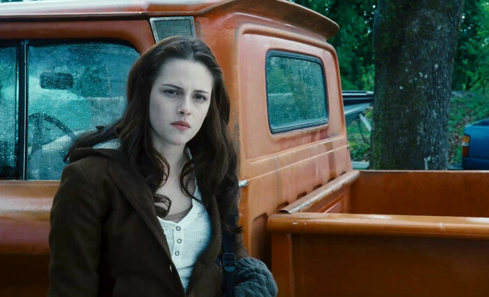Young woman standing beside an old orange pickup truck, illustrating unrealistic women movie tropes in film scenes.