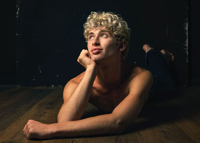 Young man with curly blonde hair lying on wooden floor, representing Missouri&rsquo;s first male homecoming queen facing renewed hate.