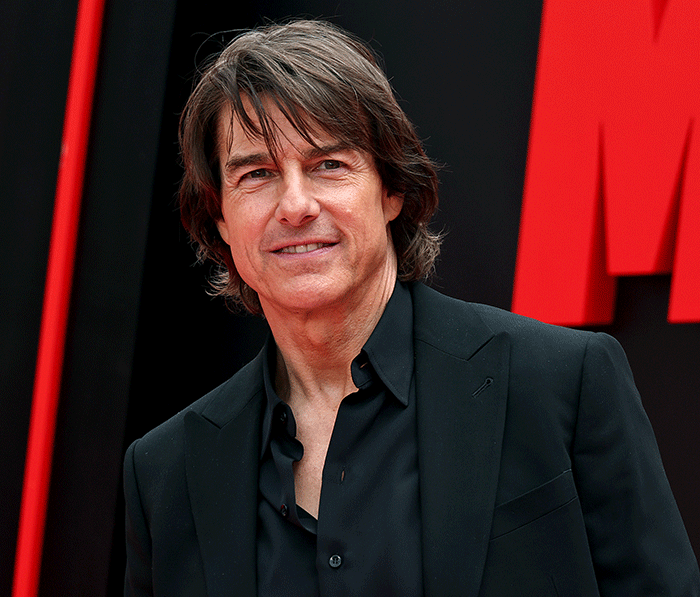 Tom Cruise smiling on red carpet wearing a black suit jacket and shirt at a movie premiere event. Tom Cruise smiling on red carpet wearing a black suit jacket and shirt at a movie premiere event.