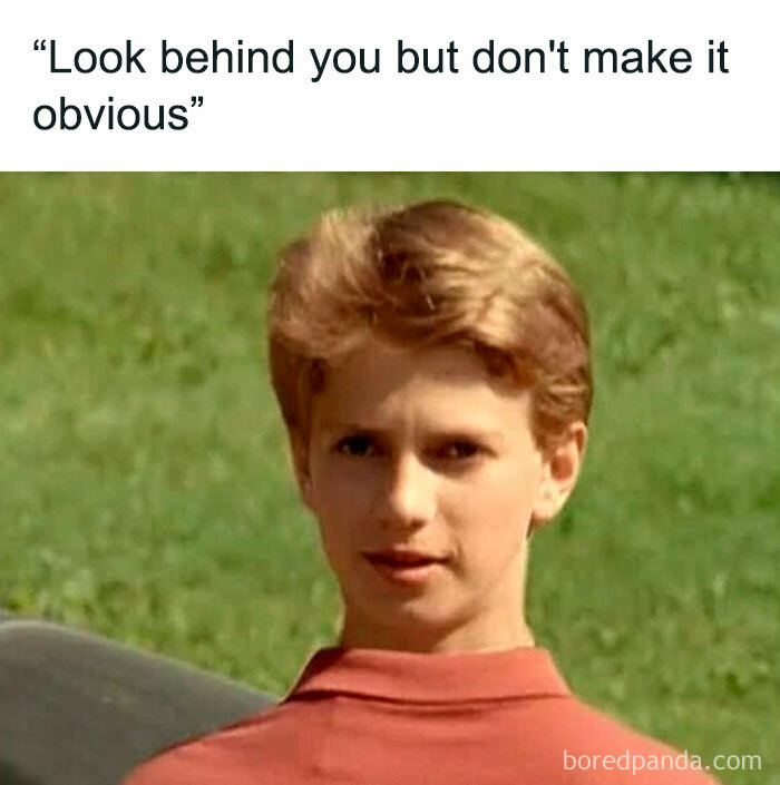 Boy in red shirt looking seriously outdoors, humorous horror movie meme caption about looking behind without making it obvious.