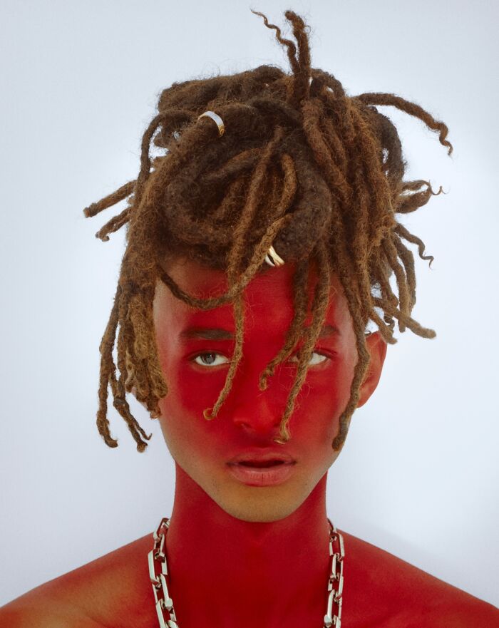 Young Nepo Baby with dreadlocks and red face paint wearing a silver chain necklace against a white background