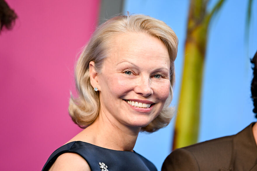 Pamela Anderson with blonde hair smiling, wearing a dark dress, related to Pamela Anderson net worth and career reinvention.