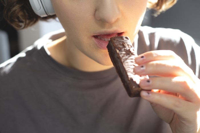 Young woman eating a chocolate bar, symbolizing parents lied about food allergies causing no contact with daughter