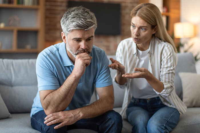 Man refusing to be step-father looks upset while woman explains, sitting on a couch in a living room.