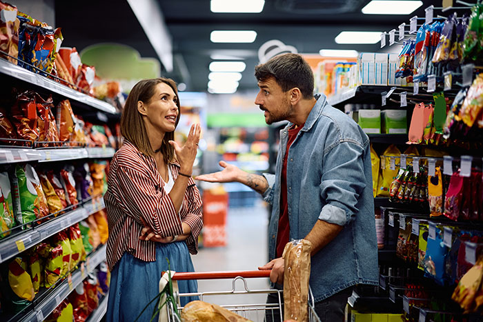 Husband and wife arguing in grocery store aisle showing tension and bullying behavior triggering past trauma.