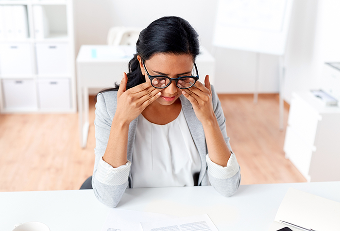 Stressed female worker in office rubbing eyes, showing exhaustion despite going above and beyond at work.