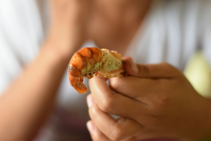 Teen holds shrimp while showing signs of an allergic reaction at a friend's house during a meal. Teen holds shrimp while showing signs of an allergic reaction at a friend's house during a meal.