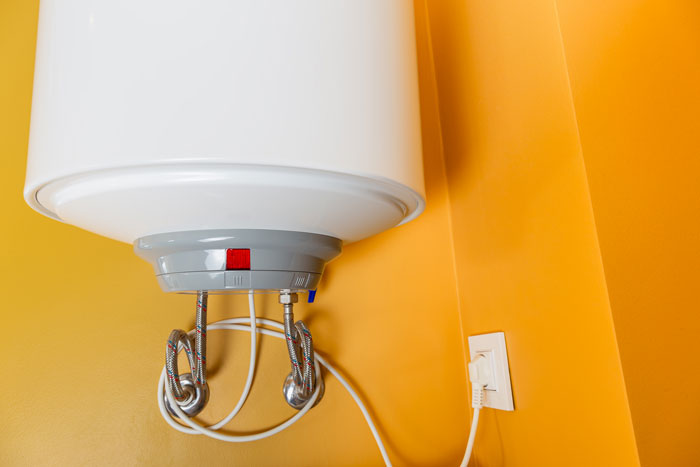 White water heater attached to a yellow wall with pipes and power cord illustrating on-site landlord acts awful concept