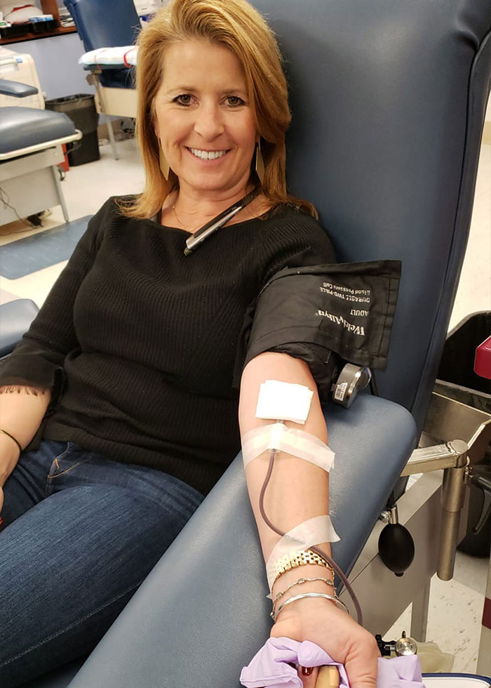 Woman smiling while donating blood, with a blood pressure cuff and needle in her arm in a medical setting