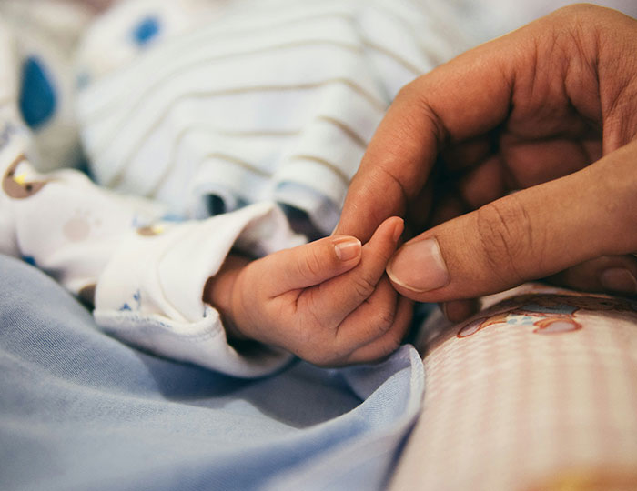 A close-up of an adult holding a newborn baby&rsquo;s hand, illustrating family bonds amid UK health guidance controversy.