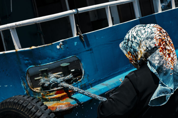 Person wearing a patterned headscarf working on a weathered blue boat in a stunning street photography shot capturing life moments.