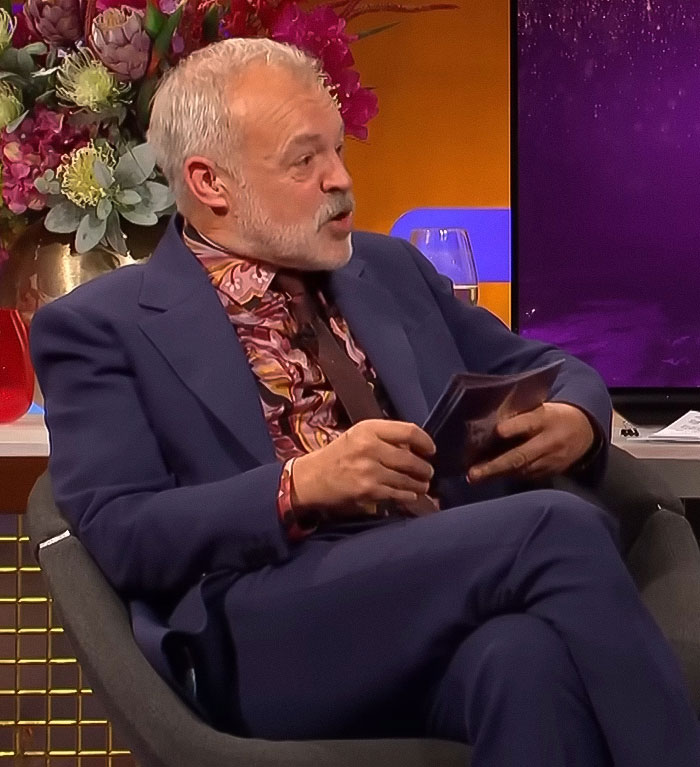 Graham Norton seated in a suit during a talk show segment, allegedly cutting off an insensitive question. Graham Norton seated in a suit during a talk show segment, allegedly cutting off an insensitive question.