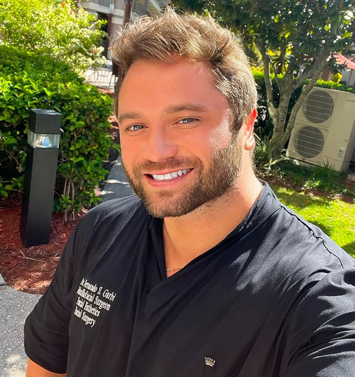 Smiling man outdoors wearing black shirt with text about facial surgeon, related to fox eyes surgery complications.