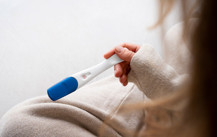 Person in beige holding positive pregnancy test, relating to daycare workers and family secrets topic.