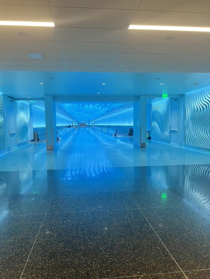 Blue-lit liminal space corridor with reflective floor and wave-patterned walls, creating a beautiful yet unnerving atmosphere.