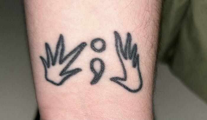 Close-up of an unusual wrist tattoo featuring abstract hand shapes and a semicolon, showcasing unique tattoo designs.